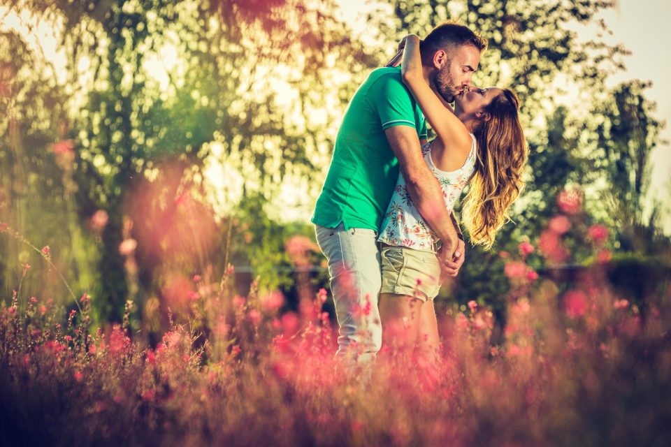 Una pareja se abraza y se besa entre flores en un parque.