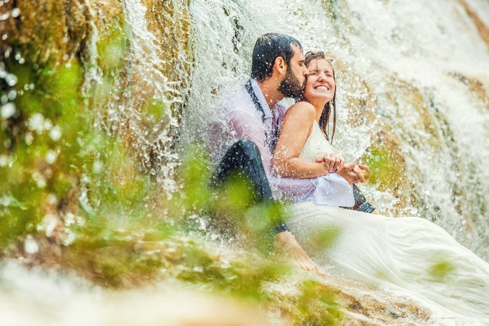 Una pareja se abraza y se besa junto a una cascada.