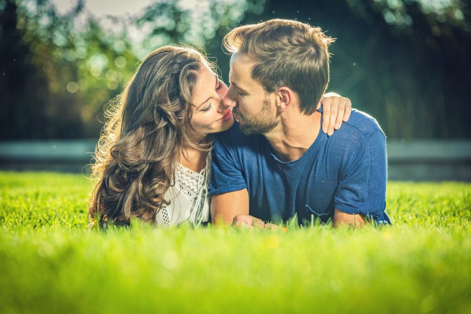 Una pareja se besa sentada sobre la hierba de un parque.