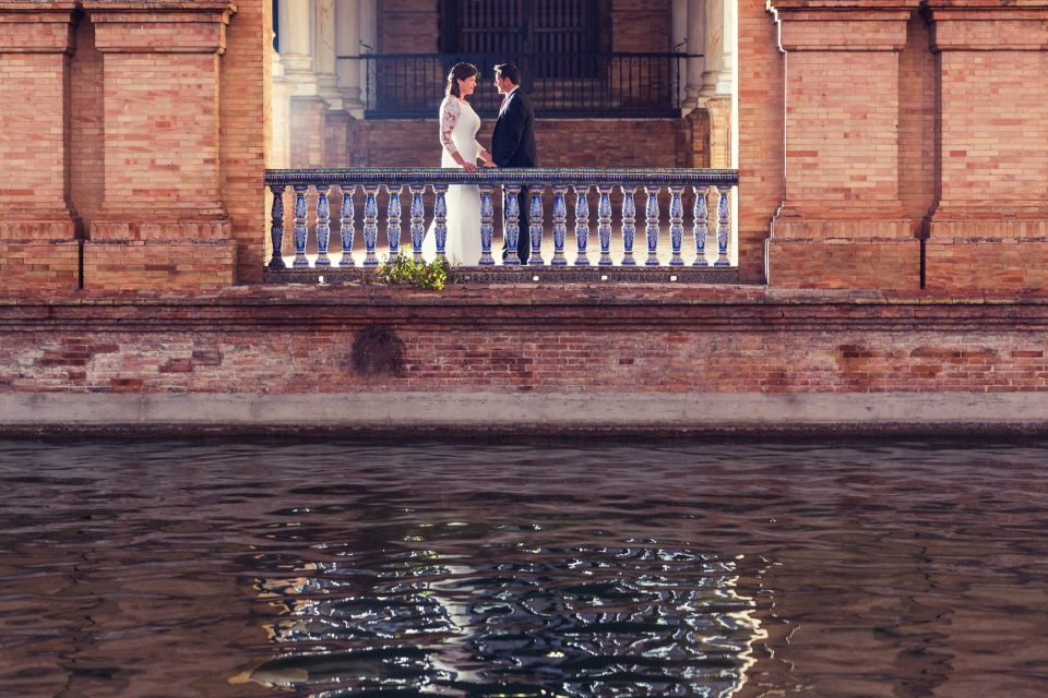 A couple face each other on a balcony with a blue-and-white tiled balustrade.