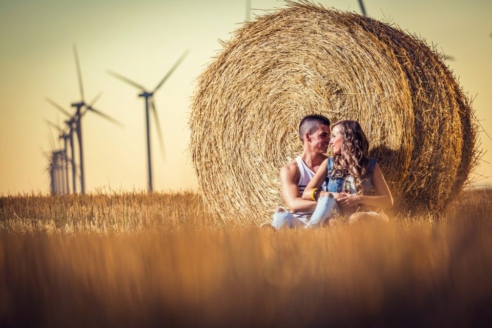 Una pareja sentada y abrazada junto a una gran bala de paja en un campo de cultivo.