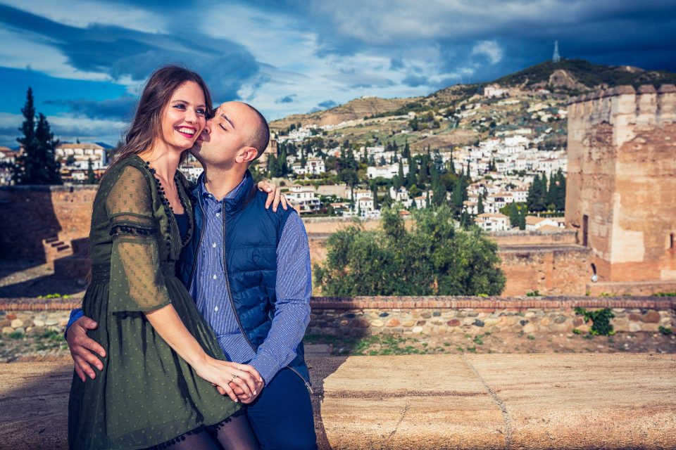 A couple smile and embrace as one person gently kisses the other's cheek.