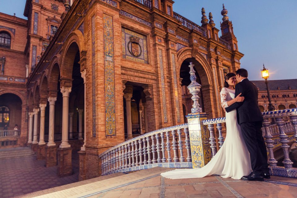 A couple dressed for their wedding pose embracing on a staircase decorated with blue and white tiles.