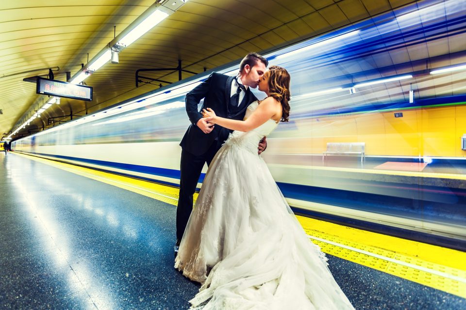 Una pareja vestida de boda se besa en el andén de una estación de metro.