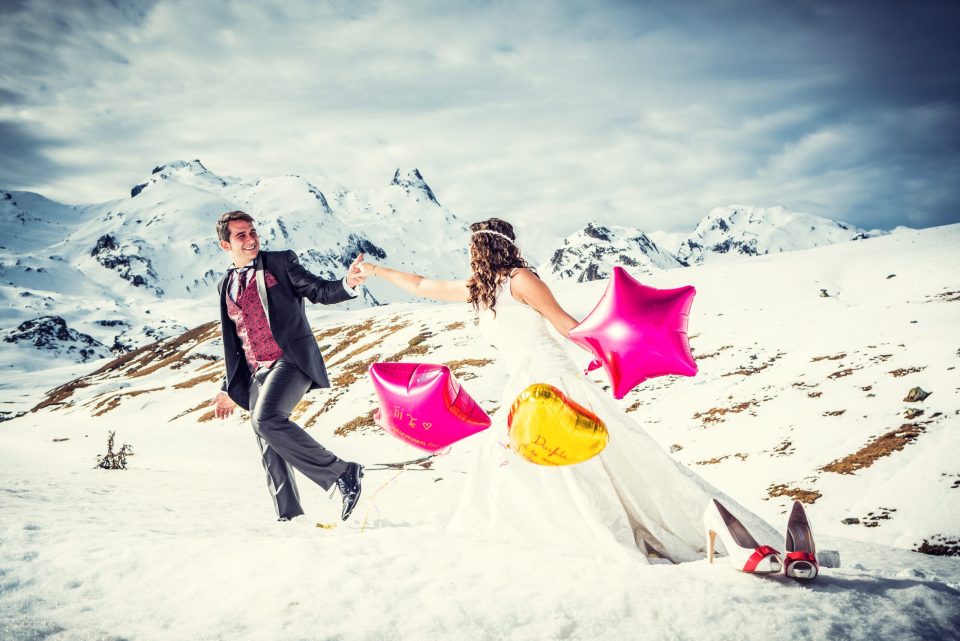 Una pareja vestida de novio y novia aparece sobre un paisaje nevado de montaña.
