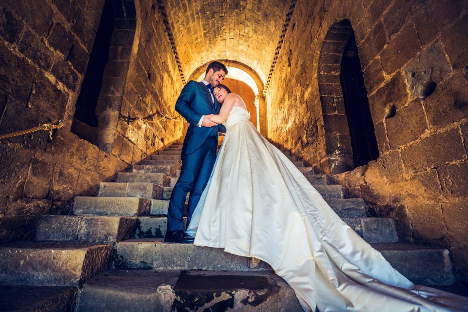 A couple dressed for a wedding pose embracing on an old stone staircase.