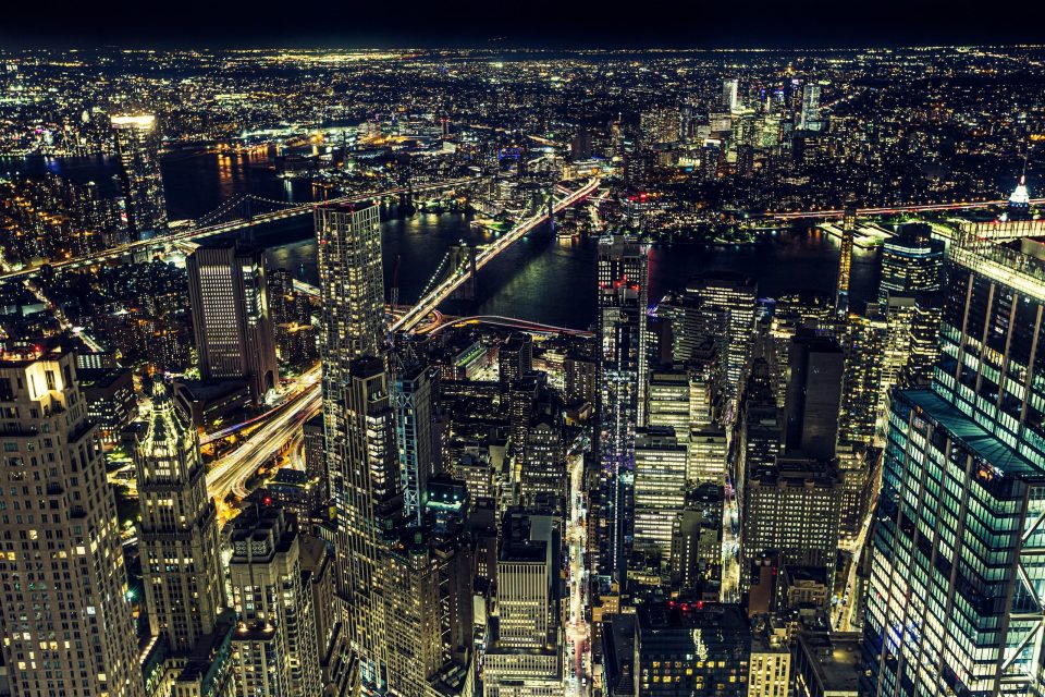 Night-time aerial view of a large city with numerous illuminated buildings.