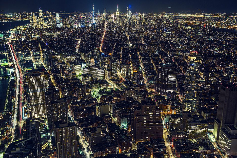 An aerial night view shows a large city with numerous illuminated buildings.