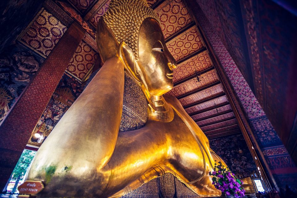A large golden reclining Buddha statue is seen from close up and at a low angle inside a temple.