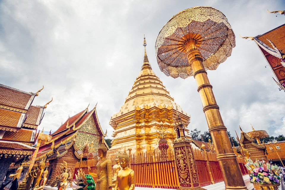 An ornate Buddhist complex has a large golden stupa in the centre and decorated roofs on both sides.