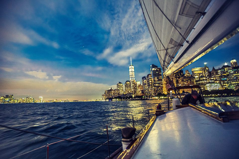 This is a night view from a boat, with water in the foreground and a city skyline of illuminated skyscrapers in the background.