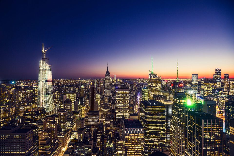 Panoramic view of a cityscape at dusk, with numerous skyscrapers and illuminated buildings.