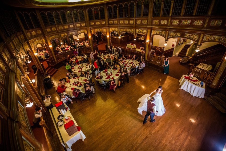 Panoramic view from an elevated level of an ornate reception room with wood panelling, decorative arches and parquet flooring.